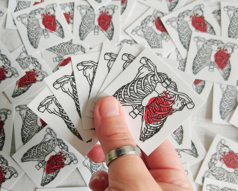 May include: A sheet of temporary tattoos featuring a black and white anatomical heart with a red heart inside. The tattoos are on a white background and are arranged in a stack.