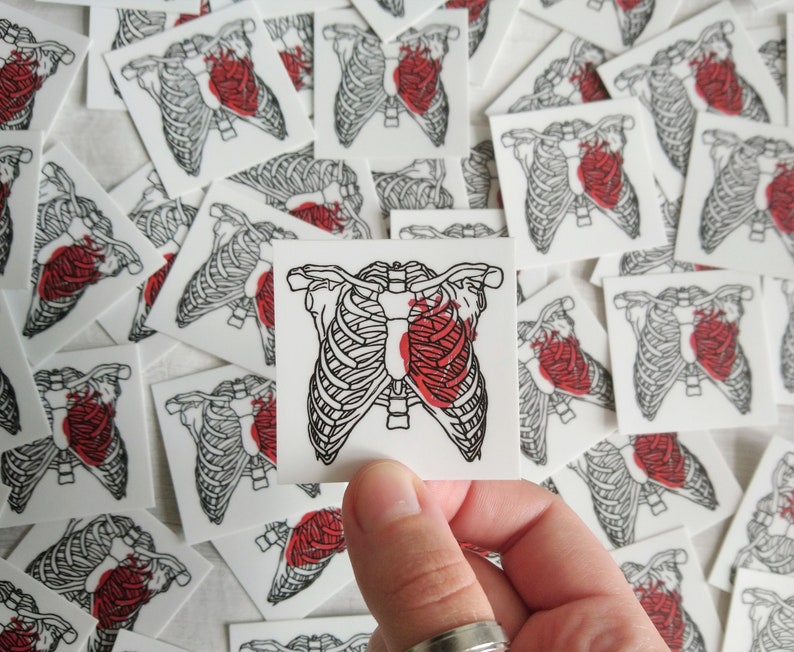 May include: A set of small, white square stickers with a black and white illustration of a ribcage with a red heart inside. The heart is partially filled with red, as if it is bleeding.