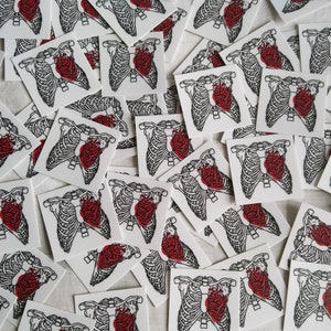 May include: A collection of white stickers with black outlines of a ribcage and a red heart inside. The stickers are scattered on a white surface.