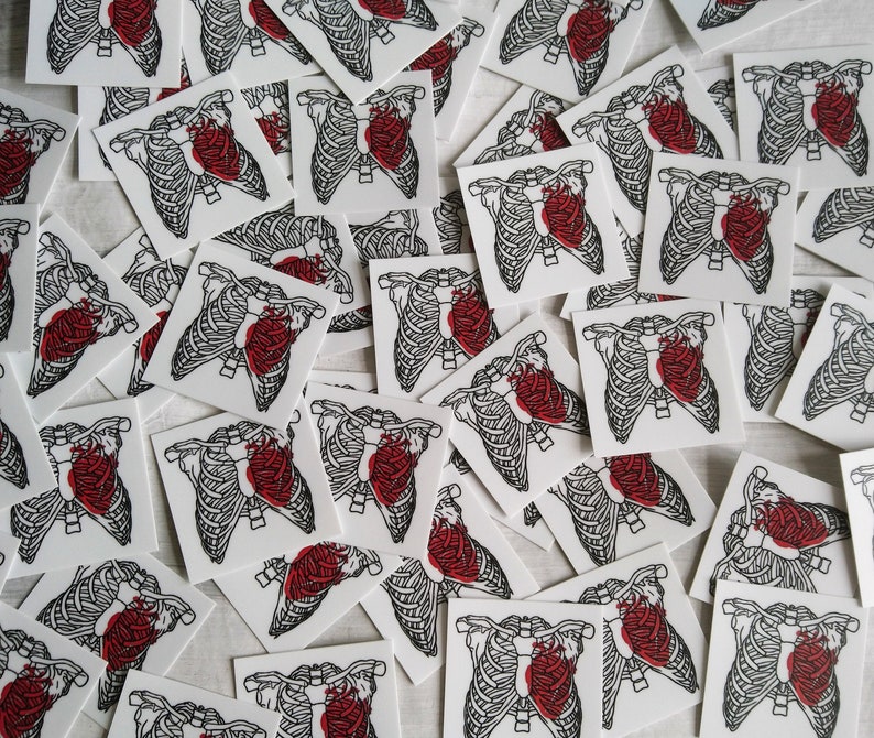 May include: A collection of white stickers with black outlines of a ribcage and a red heart inside. The stickers are scattered on a white surface.