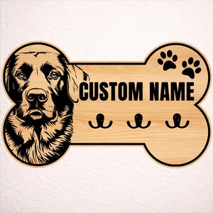May include: A wooden dog bone-shaped wall hook with a black and white dog portrait on the left side. The text "CUSTOM NAME" is in the center, with three black hooks below. Two paw prints are on the right.