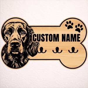 May include: Wooden dog bone-shaped sign with a detailed black and white dog portrait on the left. The sign has the text "CUSTOM NAME" and three black hooks below. Two paw prints are on the right side.