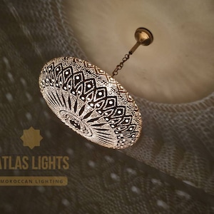 May include: A gold Moroccan pendant light with a decorative, intricate, geometric pattern. The light is hanging from a chain and has a round, dome-shaped shade.