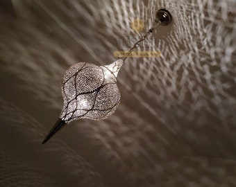 May include: A silver Moroccan pendant light with a delicate, intricate design. The light is shaped like a teardrop and hangs from a chain.