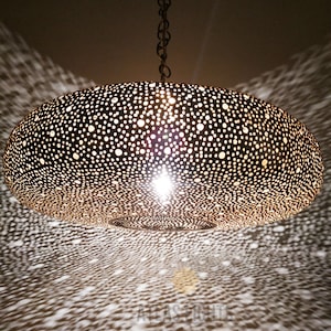 May include: A large, round, gold-colored Moroccan pendant light fixture with a decorative, intricate, perforated pattern. The light fixture is hanging from a chain.