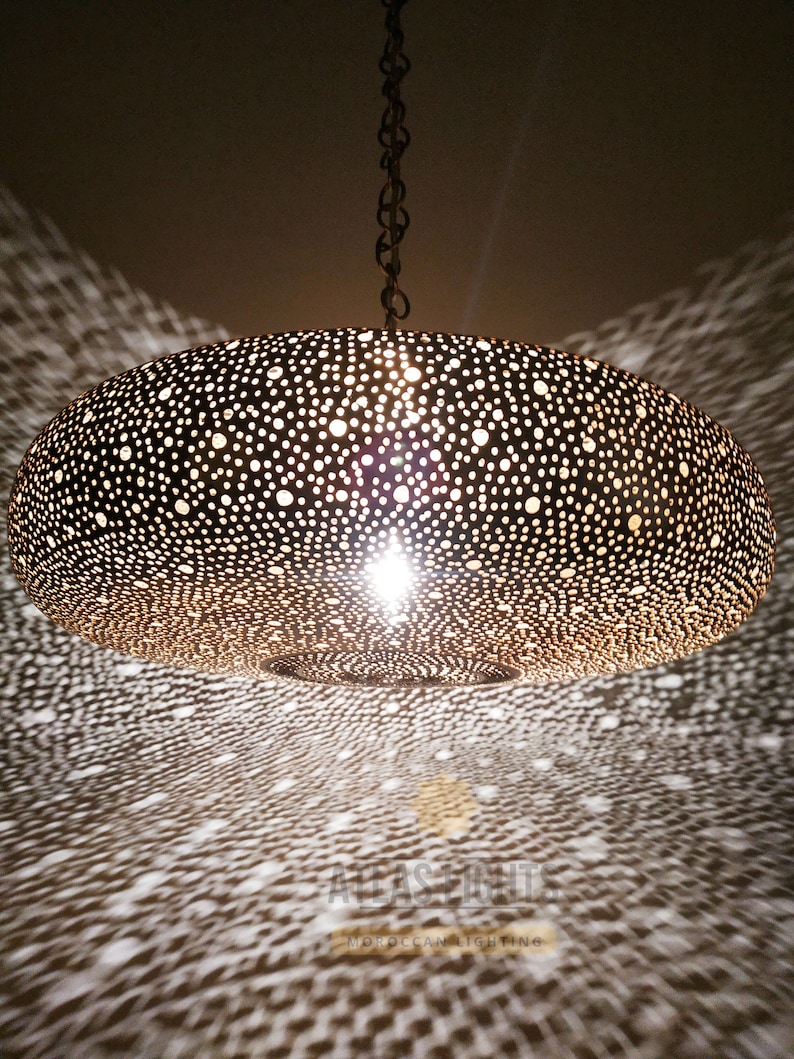 May include: A large, round, gold-colored Moroccan pendant light fixture with a decorative, intricate, perforated pattern. The light fixture is hanging from a chain.