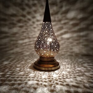 May include: A brass table lamp with a decorative, pierced, teardrop-shaped shade. The lamp has a round base and a pointed finial.