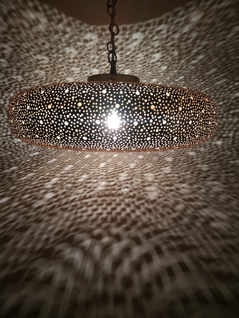 Moroccan Brass Lantern Chandelier with Stunning Light Pattern
Bring the magic of Marrakesh into your home with this magnificent, handcrafted Moroccan Brass Pendant Light. Known for its exquisite craftsmanship, this lamp is meticulously hand-punched, allowing light to filter through a myriad of small perforations to cast an immersive, spectacular, starburst pattern of light and shadow on your walls and ceiling.