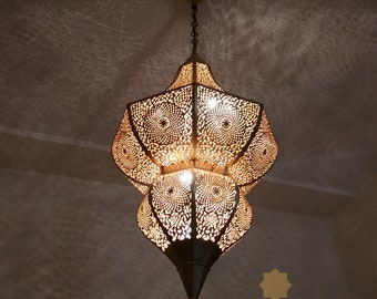 May include: A large, ornate, brass Moroccan pendant light with intricate cut-out designs. The light is hanging from a chain and is illuminated, casting a warm glow.
