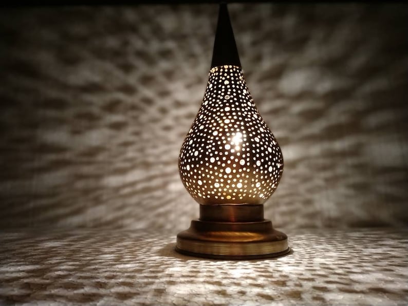 May include: A brass table lamp with a pearlescent finish and a pierced design. The lamp has a round base and a teardrop-shaped shade.