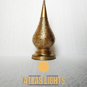 May include: A gold metal Moroccan lantern with a decorative pierced design. The lantern has a pointed top and a round base. The lantern is on a white background.  Atlas Lights Moroccan Lighting.