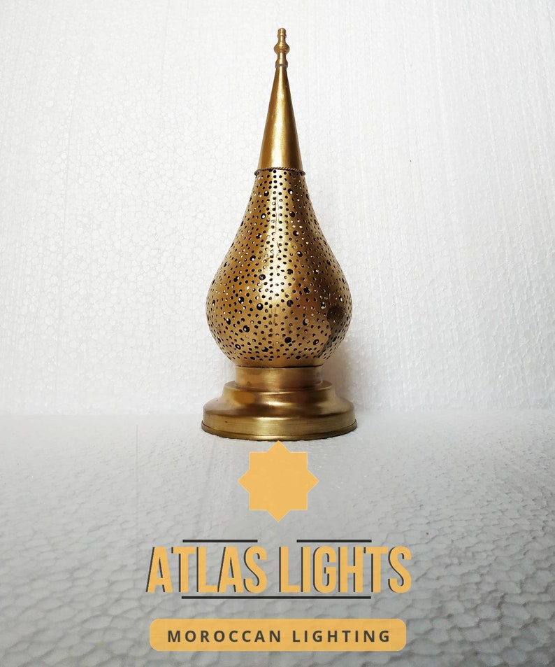 May include: A gold metal Moroccan lantern with a decorative pierced design. The lantern has a pointed top and a round base. The lantern is on a white background.  Atlas Lights Moroccan Lighting.
