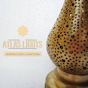 May include: A gold Moroccan lantern with a round, perforated design. The lantern is on a white background with the text "ATLAS LIGHTS" and "MOROCCAN LIGHTING" below it.