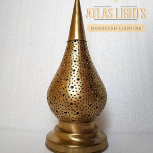 May include: A gold metal Moroccan lantern with a decorative, perforated design. The lantern has a pointed top and a round base.