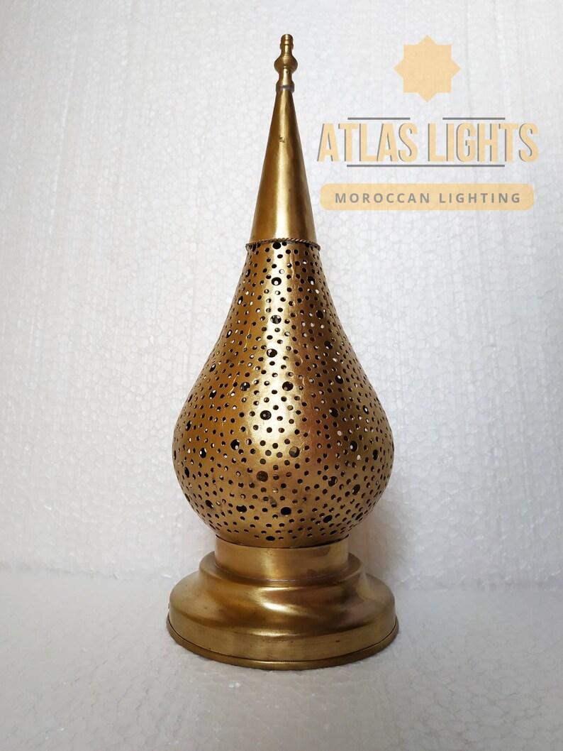 May include: A gold metal Moroccan lantern with a decorative, perforated design. The lantern has a pointed top and a round base.
