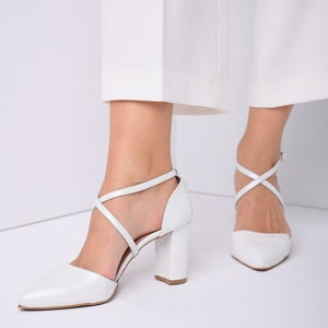 May include: White leather heeled shoes with criss-cross straps and a pointed toe.