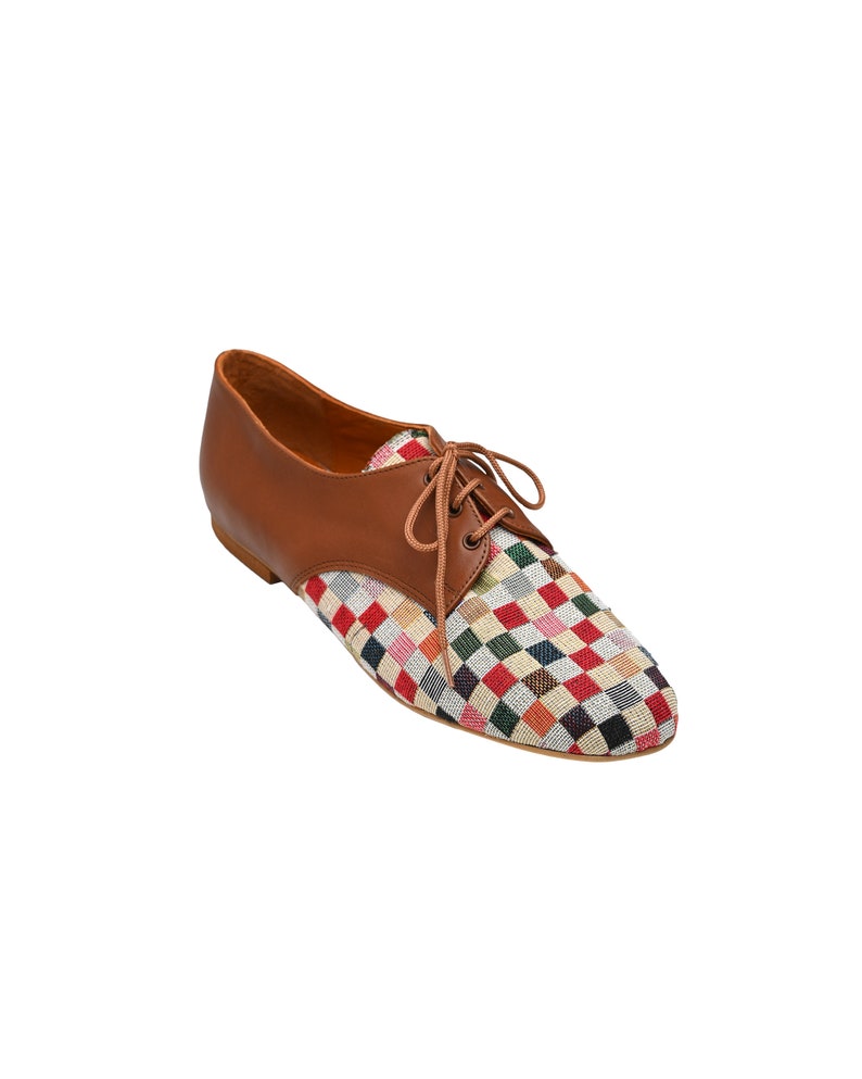 May include: A brown leather oxford shoe with a colorful checkered fabric toe. The shoe has brown laces and a low heel. The checkered pattern includes red, green, blue, and yellow squares.