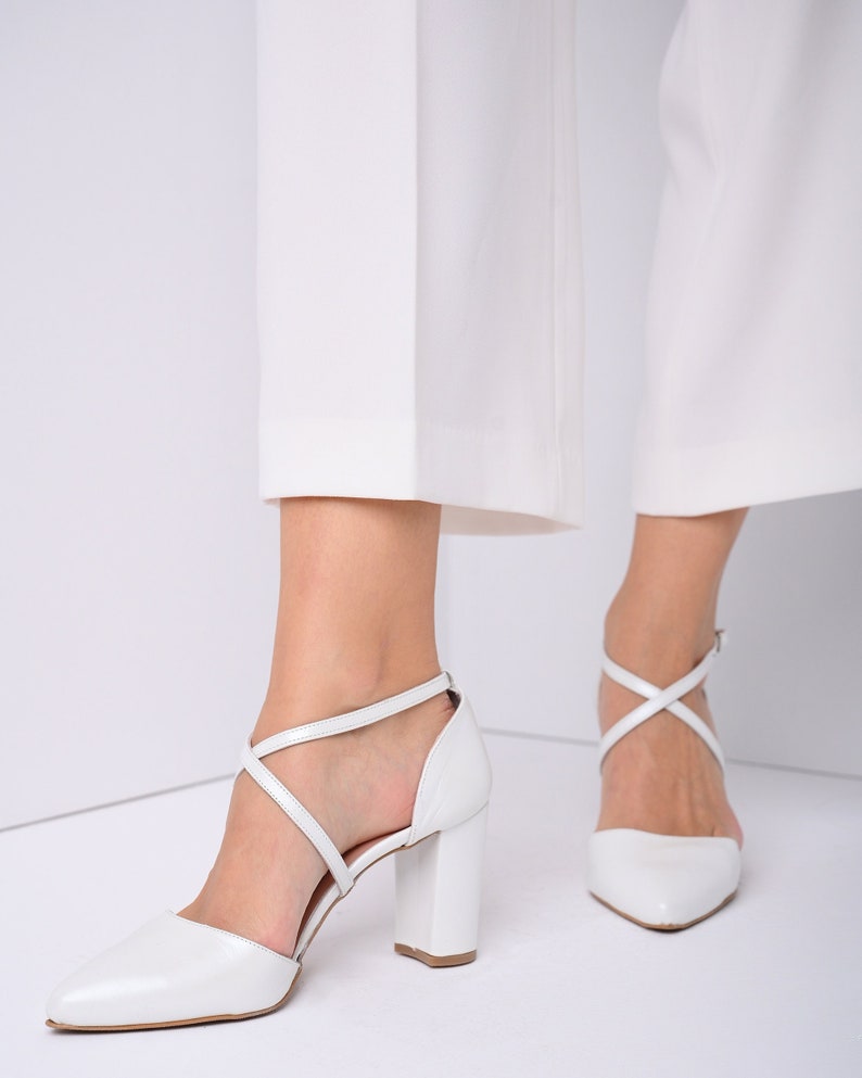 May include: White leather heeled shoes with criss-cross straps and a pointed toe.