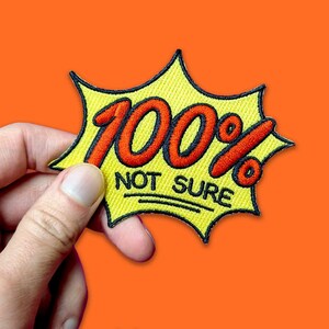 Könnte beinhalten: Ein gelber gestickter Aufnäher mit einem roten 100% und dem Text "NOT SURE" in Schwarz.