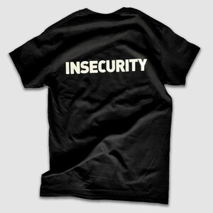 Op de afbeelding: Zwart T-shirt met het woord "INSECURITY" in wit op de rug.