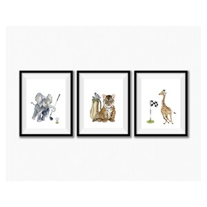 May include: A set of three framed prints featuring animal illustrations playing golf. The first print shows an elephant swinging a golf club, the second print shows a tiger holding a golf bag, and the third print shows a giraffe running towards a golf flag.