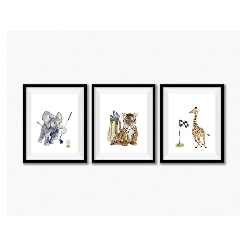 May include: A set of three framed prints featuring animal illustrations playing golf. The first print shows an elephant swinging a golf club, the second print shows a tiger holding a golf bag, and the third print shows a giraffe running towards a golf flag.