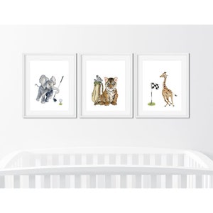 May include: Three framed prints featuring watercolor illustrations of animals playing golf. The first print shows an elephant swinging a golf club, the second print shows a tiger holding a golf bag, and the third print shows a giraffe running towards a checkered flag.