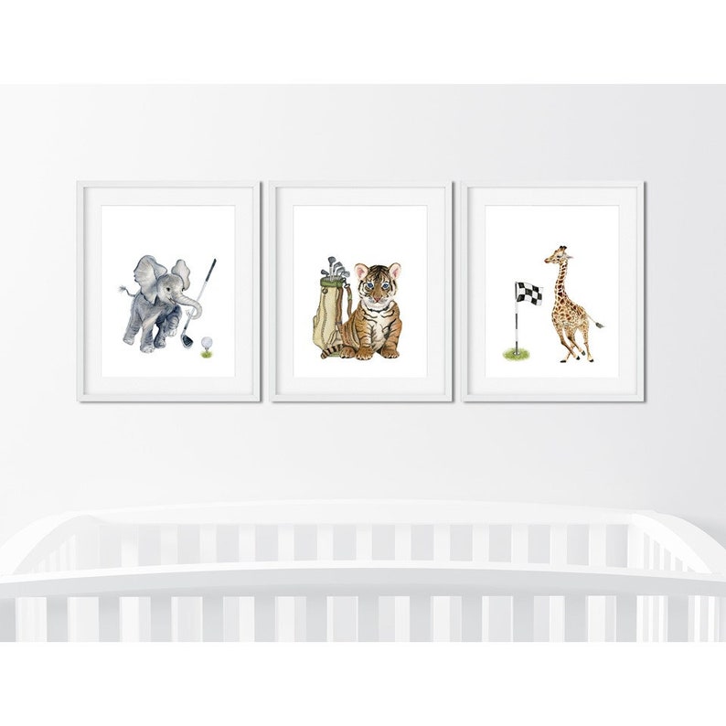 May include: Three framed prints featuring watercolor illustrations of animals playing golf. The first print shows an elephant swinging a golf club, the second print shows a tiger holding a golf bag, and the third print shows a giraffe running towards a checkered flag.