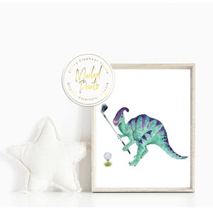 Op de afbeelding: Een aquarel van een groene dinosaurus die golf speelt. De dinosaurus houdt een golfclub vast en staat op het punt om een golfbal te slaan. De dinosaurus heeft een paarse kam op zijn kop. Het schilderij is ingelijst in een licht houten lijst.