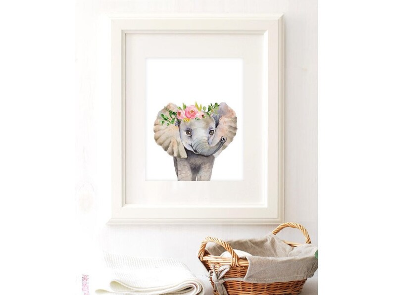 K&ouml;nnte beinhalten: Ein Aquarellbild eines Babyelefanten, das eine rosa und gr&uuml;ne Blumenkrone tr&auml;gt. Der Elefant schaut den Betrachter mit erhobenem R&uuml;ssel an. Das Bild ist in einem wei&szlig;en Rahmen gerahmt.