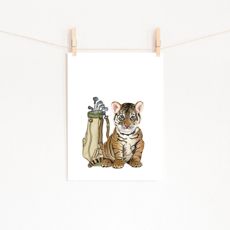 May include: A watercolor illustration of a tiger cub sitting next to a golf bag with clubs sticking out of the top.