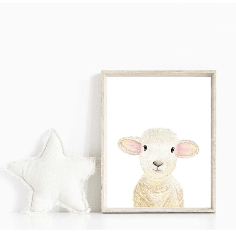 May include: A watercolor painting of a white lamb with pink ears and a light brown body. The lamb is looking directly at the viewer with a sweet expression. The painting is framed in a light wood frame.