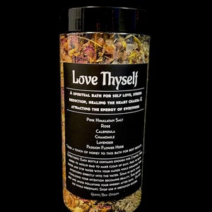 May include: A glass jar filled with pink Himalayan salt, rose petals, calendula, chamomile, lavender, and passion flower herb. The jar has a black label with the text "Love Thyself" and a description of the bath salts' benefits. The text on the label reads: "A spiritual bath for self love, stress reduction, healing the heart chakra & attracting the energy of sweetness."