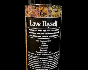 May include: A glass jar filled with pink Himalayan salt, rose petals, calendula, chamomile, lavender, and passion flower herb. The jar has a black label with the text "Love Thyself" and a description of the bath salts' benefits. The text on the label reads: "A spiritual bath for self love, stress reduction, healing the heart chakra & attracting the energy of sweetness."