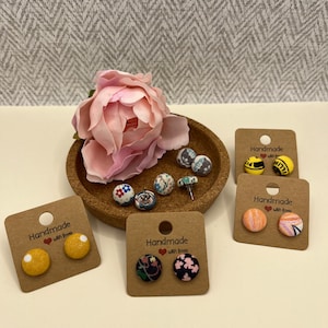 May include: Assortment of handmade fabric earrings with different patterns and colours. The earrings are displayed on brown cards with the text "Handmade with love".