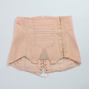 May include: A pale pink corset with a lace-up front and a zipper on the side. The corset has a textured fabric and a wide waistband.