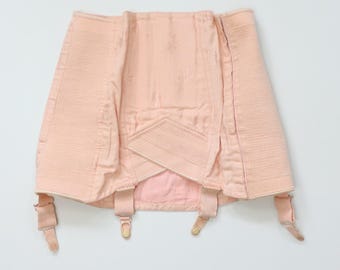 May include: A vintage pale pink corset with garter straps. The corset features a structured design with vertical and horizontal stitching, and a decorative panel at the front. The garter straps have metal clasps.