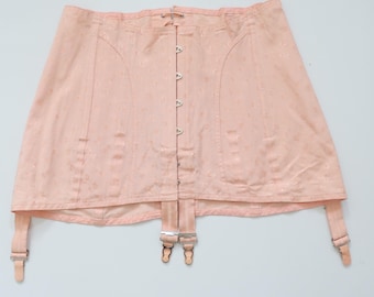 May include: A vintage pale pink corset with a floral pattern. The corset features a series of hook-and-eye closures down the front and garter straps. The garment is made of a soft, possibly satin-like material.