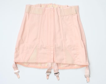 May include: A pale pink vintage garter belt with four suspender straps and metal clasps. The belt has a high waist design with beige elastic panels and a front closure. The fabric appears to be a smooth, possibly satin-like material.