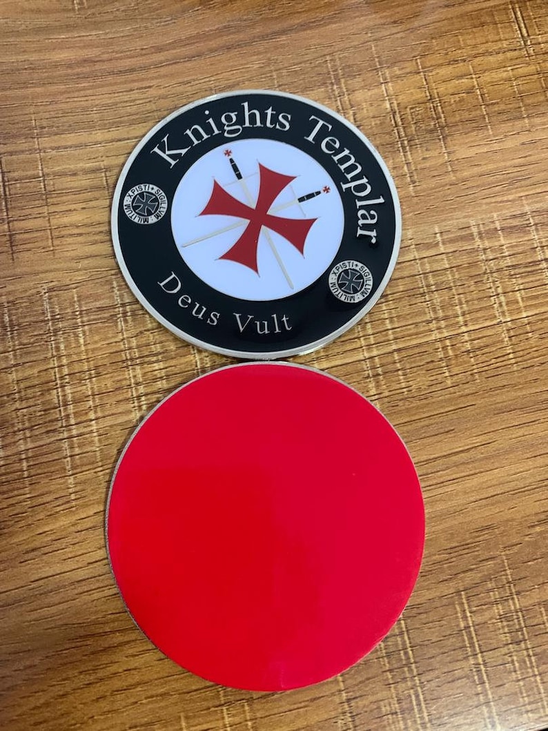 Puede incluir: Un posavasos redondo con base roja y una parte superior con las palabras "Knights Templar" alrededor de un dise&ntilde;o de cruz roja. Tambi&eacute;n est&aacute;n presentes las palabras "Deus Vult". El posavasos tiene un borde negro y est&aacute; sobre una superficie de madera.