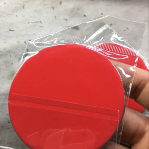 Puede incluir: Una pegatina circular de color rojo brillante con respaldo despegable, empaquetada en una funda de pl&aacute;stico transparente. La pegatina es de color rojo s&oacute;lido y vibrante, y parece nueva.