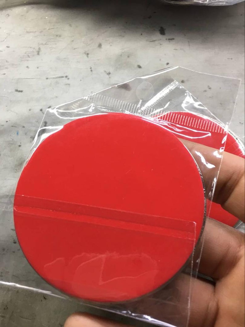 Puede incluir: Una pegatina circular de color rojo brillante con respaldo despegable, empaquetada en una funda de pl&aacute;stico transparente. La pegatina es de color rojo s&oacute;lido y vibrante, y parece nueva.