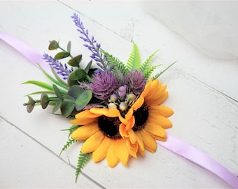 May include: A yellow sunflower with purple thistle and lavender flowers, green eucalyptus leaves, and a light purple ribbon.