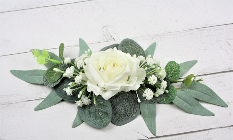 May include: A white rose with green eucalyptus leaves and small white flowers.