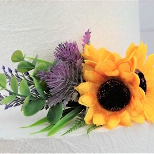May include: A wedding cake topper featuring a bouquet of yellow sunflowers, purple thistle, lavender sprigs, and green foliage.