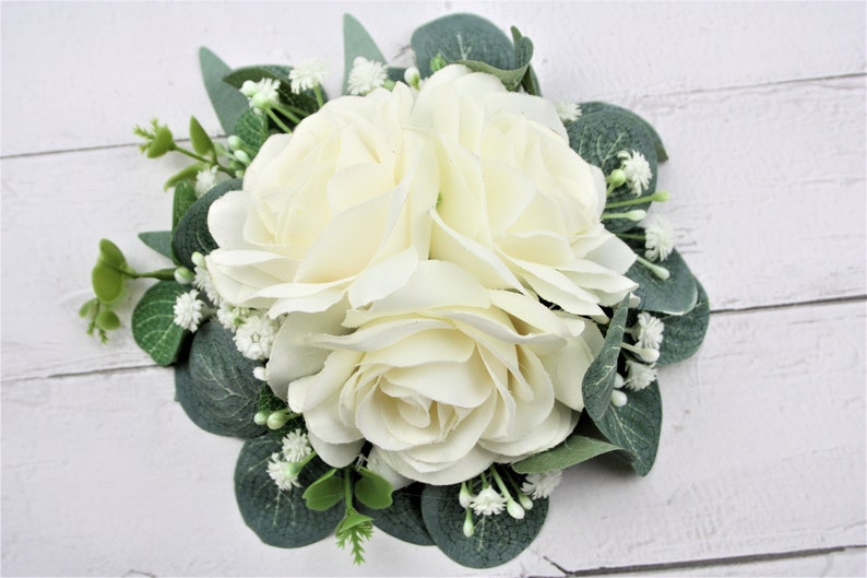 May include: A bouquet of three ivory roses with green leaves and small white flowers.