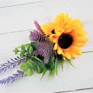 May include: A bouquet of artificial flowers featuring a yellow sunflower, purple thistle, and lavender sprigs with green eucalyptus leaves.