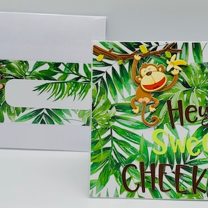May include: A greeting card with a jungle theme. The card features a monkey holding a banana and the text "Hey Sweet Cheeks!" on a green and white background.