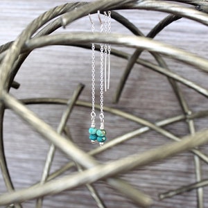 May include: A pair of silver dangle earrings with turquoise beads. The earrings are hanging from a metal stand.