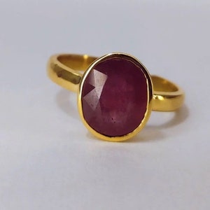 以下が含まれることがあります： 大きな楕円形のルビーの宝石が付いた金の指輪。ルビーは濃い赤色で、ファセットカットされています。